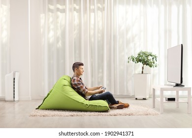 Profile Shot Of A Male Teenager Sitting On A Bean Bag Armchair And Playing Video Games At Home