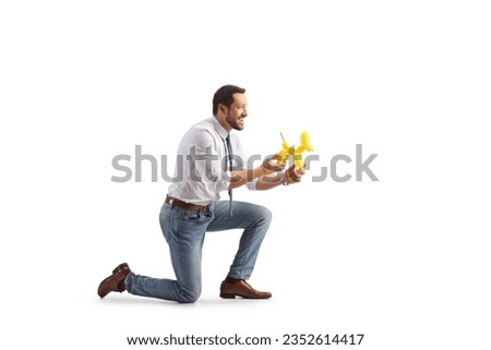 Profile shot of a man kneeling and holding a dog made from a balloon isolated on white background