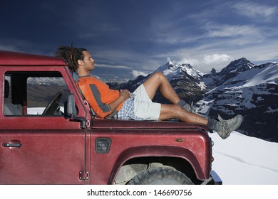 Profile shot of man relaxing on car hood against mountains during winter - Powered by Shutterstock