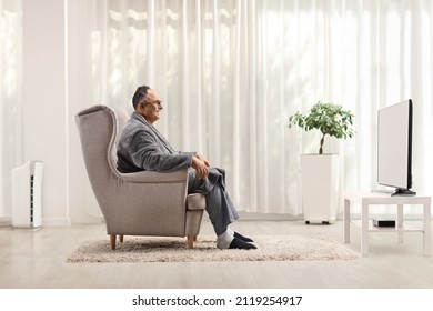 Profile Shot Of A Mature Man In A Bathrobe Sitting In An Armchair And Watching Tv At Home