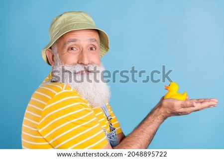 Profile side photo of aged man happy positive smile hold rubber duckling toy isolated over blue color background