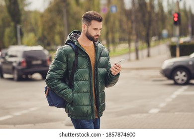 Profile Side Photo Of Cute Confident Young Guy Dressed Green Coat Rucksack Walking Chatting Modern Gadget Outdoors City Street