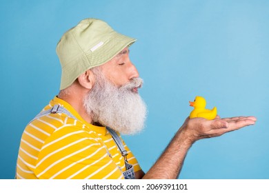 Profile side photo of senior man pouted lips kiss hold hands duck swim bath isolated over blue color background