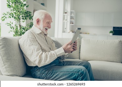 Profile Side View Of Cheerful Cheery Positive Old Man Sitting On Divan Holding In Hands Ebook Browsing High Fast Speed Internet In White Light Modern Interior