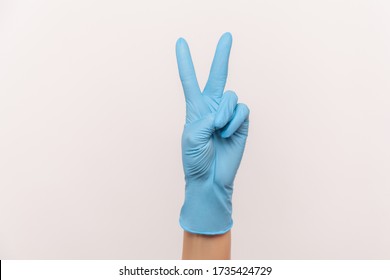 Profile side view closeup of human hand in blue surgical gloves showing victory, peace sign or number 2 with fingers. indoor, studio shot, isolated on gray background.