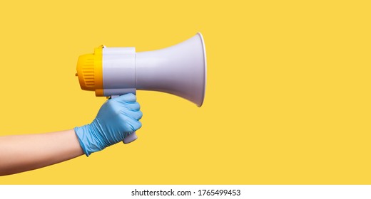 Profile Side View Closeup Of Human Hand In Blue Surgical Gloves Holding Megaphone. Indoor, Studio Shot, Isolated On Yellow Background.