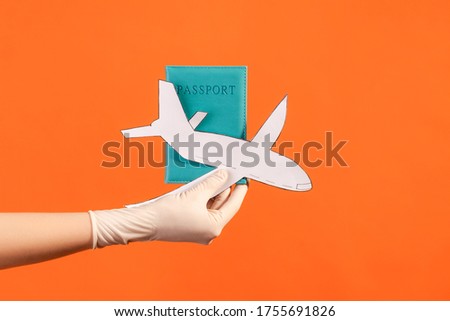 Profile side view closeup of human hand in white surgical gloves holding passport and airplane paper. indoor, studio shot, isolated on orange background.