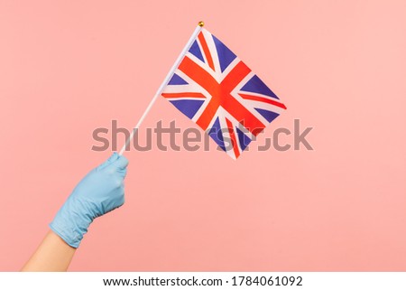 Profile side view closeup of human hand in blue surgical gloves holding flag of a constituent unit of the United Kingdom. June 4: British Independence Day. indoor shot, isolated on pink background.