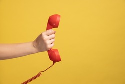 Profile Side View Closeup Of Woman Hand Holding And Showing Red Call Telephone Handset Receiver. Indoor Studio Shot Isolated On Yellow Background.