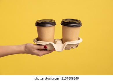 Profile Side View Closeup Of Woman Hand Holding And Showing Cup Of Hot Takeaway Mug Drink In Hand, Coffee Break At Work. Indoor Studio Shot Isolated On Yellow Background.