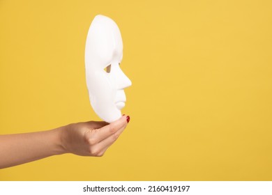 Profile Side View Closeup Of Woman Hand Holding White Facial Mask Model, Hiding Personality. Indoor Studio Shot Isolated On Yellow Background.