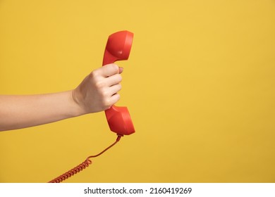 Profile side view closeup of woman hand holding and showing red call telephone handset receiver. Indoor studio shot isolated on yellow background.