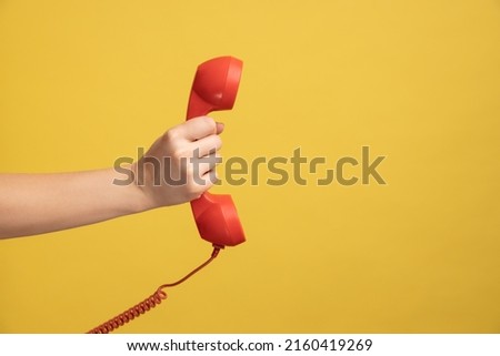 Profile side view closeup of woman hand holding and showing red call telephone handset receiver. Indoor studio shot isolated on yellow background.