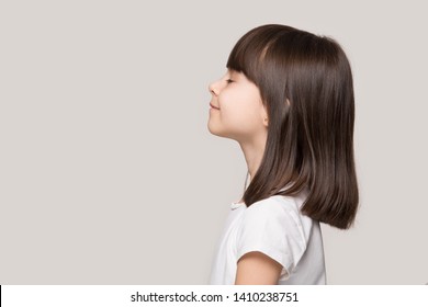 Profile side view face brown-haired little girl standing isolated on beige studio background, preschool kid do deep breath enjoy fresh air or dreaming fill with energy feeling healthy and good concept