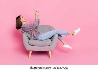 Profile side view portrait of attractive cheerful girl sitting in armchair using device isolated over pink pastel color background - Shutterstock ID 2143309903