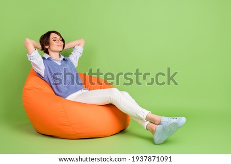 Profile side view portrait of attractive dreamy girl sitting in bag chair resting isolated over green color background
