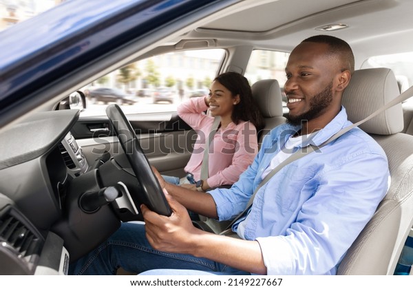 Profile side view portrait of happy black man and\
woman going on summer vacation by car. Cheerful millennial African\
American couple sitting in new auto, looking at road, making test\
drive in the city