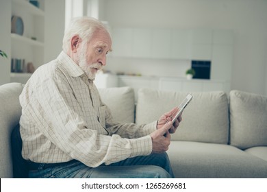 Profile Side View Portrait Of Nice Shocked Old Man Sitting On Divan Holding In Hands E-book Reading Literature Online In White Light Modern Interior