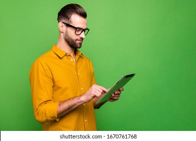 Profile side view portrait of nice attractive focused content guy in formal shirt holding in hand using digital tablet 5g connection isolated on bright vivid shine vibrant green color background
