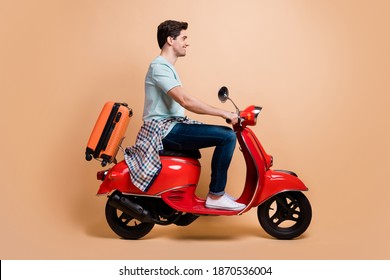 Profile Side View Portrait Of Nice Cheerful Guy Driving Moped Carrying Bag Departure Abroad Isolated Over Beige Pastel Color Background