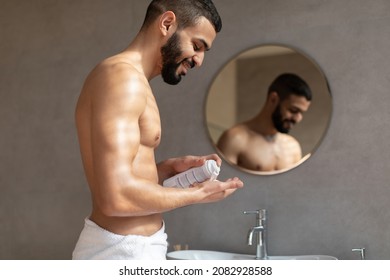 Profile Side View Portrait Of Smiling Shirtless Guy Applying Shaving Foam From Bottle Onto His Hand Palm, Cheerful Man Standing Near Mirror In Bathroom Indoors. Male Morning Self-Care Beauty Routine