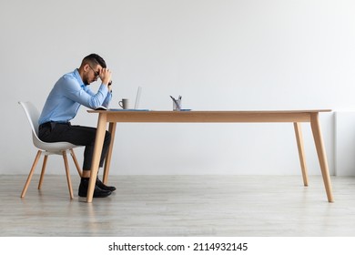 Profile Side View Of Young Middle Eastern Man Suffering From Headache At Workplace, Having Problems Thinking About Troubles. Stressed Guy In Glasses Sitting At Desk Using Computer, Free Copy Space