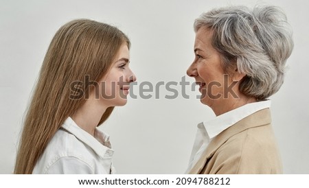 Profile of smiling caucasian granddaughter and grandmother looking at each other. Age and generation concept. Idea of family relationship. Teenage girl and senior woman on white background in studio
