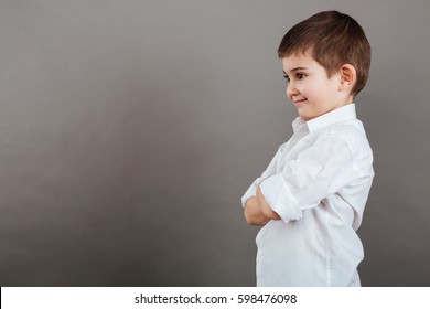 Profile Of Smiling Little Boy Standing With Arms Crossed Over Grey Background