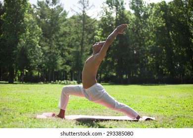 Profile of sporty Indian young man working out on grass in park, doing yoga, fitness, pilates training, lunge exercise, High Crescent Pose, warrior 1, sun salutation complex, full length