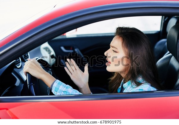 Profile of stressed woman\
driving red car, stress while driving. Woman looking ahead\
nervously, traffic jams. Head and shoulders of brunette woman\
inside car