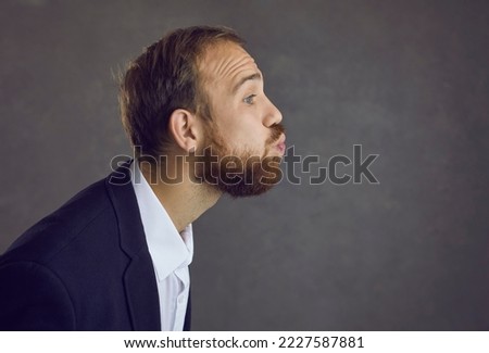 Profile view of an adult bearded man with pursed lips waiting for a kiss while standing on a gray background. Close up of a funny man in a suit who is ready to take a kiss. Concept of human feelings.