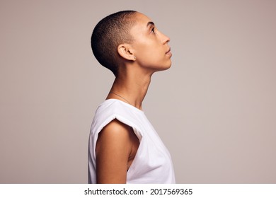 Profile view of an androgynous woman with shaved head. Young female looking away against colored background. - Shutterstock ID 2017569365