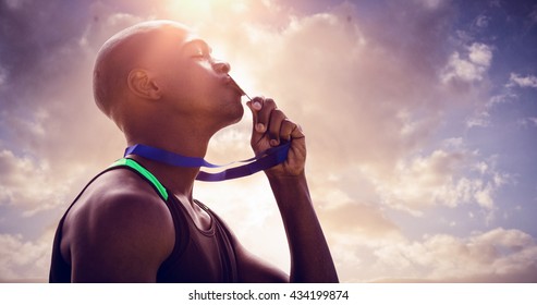 Profile view of athletic man kissing his gold medal against cloudy sky - Powered by Shutterstock