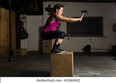Profile view of an athletic young woman jumping onto a box in a cross-training gym