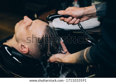 Profile view of bearded man getting his hair washed and his head massaged in hair salon. Cleaning head barber's. Barber men washing client's hair in barbershop or beaty salon.