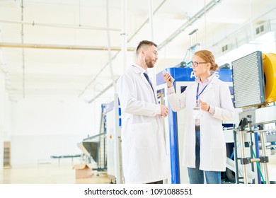 Profile View Of Beautiful Journalist Wearing Eyeglasses And White Coat Standing At Spacious Production Department Of Modern Soy Milk Factory And Interviewing Bearded Technologist