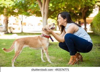 Profile View Of A Beautiful Young Woman Petting Her Dog And Giving It A Kiss At A Park