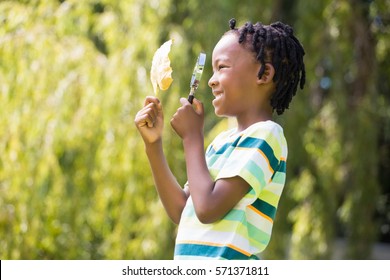 Profile View Of Boy Looking At Leaf Through Magnifying Glass In Park