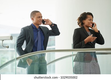 Profile View Of Busy African American Managers In Formalwear Discussing Order Details With Their Customers While Going Up Escalator In Modern Office Lobby