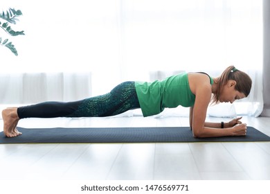 Profile View Of Concentrated And Serious Young Woman Standing In Plank Pose On Fitness Mat, Training At Home