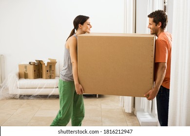 Profile View Of Couple Face To Face Moving Large Cardboard Box In New House.