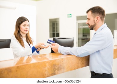 Profile View Of A Cute Receptionist Receiving A Credit Card Payment At A Front Desk In A Clinic