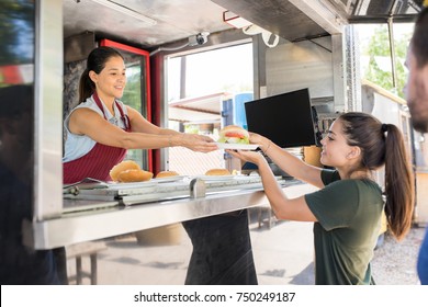 Profile view of a food truck worker handing over a hamburger to a customer and smiling - Powered by Shutterstock