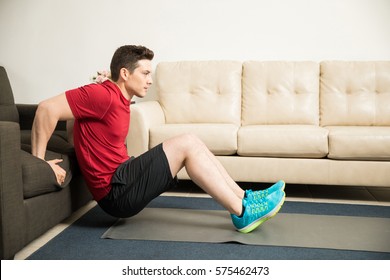 Profile view of a good looking athletic young man doing tricep dips leaning on a couch at home - Powered by Shutterstock