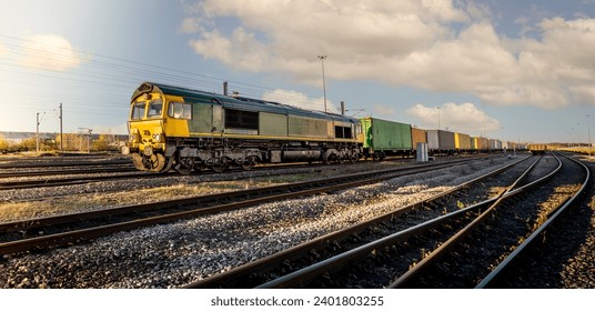 Profile view of a goods train with Intermodal wagons full of shipping container boxes for import and export in a yard or sidings