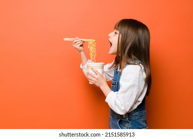 Profile View Of A Little Girl Opening A Big Mouth And Eating Noodles With Chopsticks In A Studio