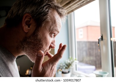 A Profile View Of A Man Licking His Fingers After Eating In The Kitchen While Looking Out The Window.