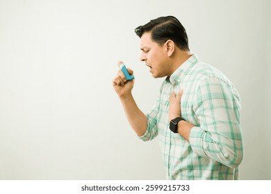 Profile view of a man using blue asthma inhaler while experiencing breathing difficulty during medical episode