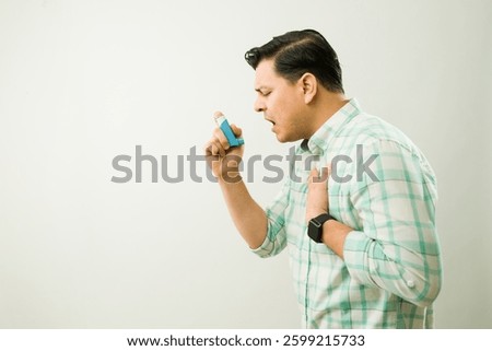 Profile view of a man using blue asthma inhaler while experiencing breathing difficulty during medical episode