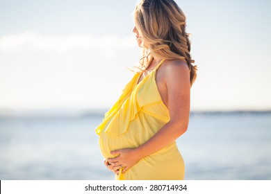 Profile view of pregnant woman with long hair in yellow dress on the beach
